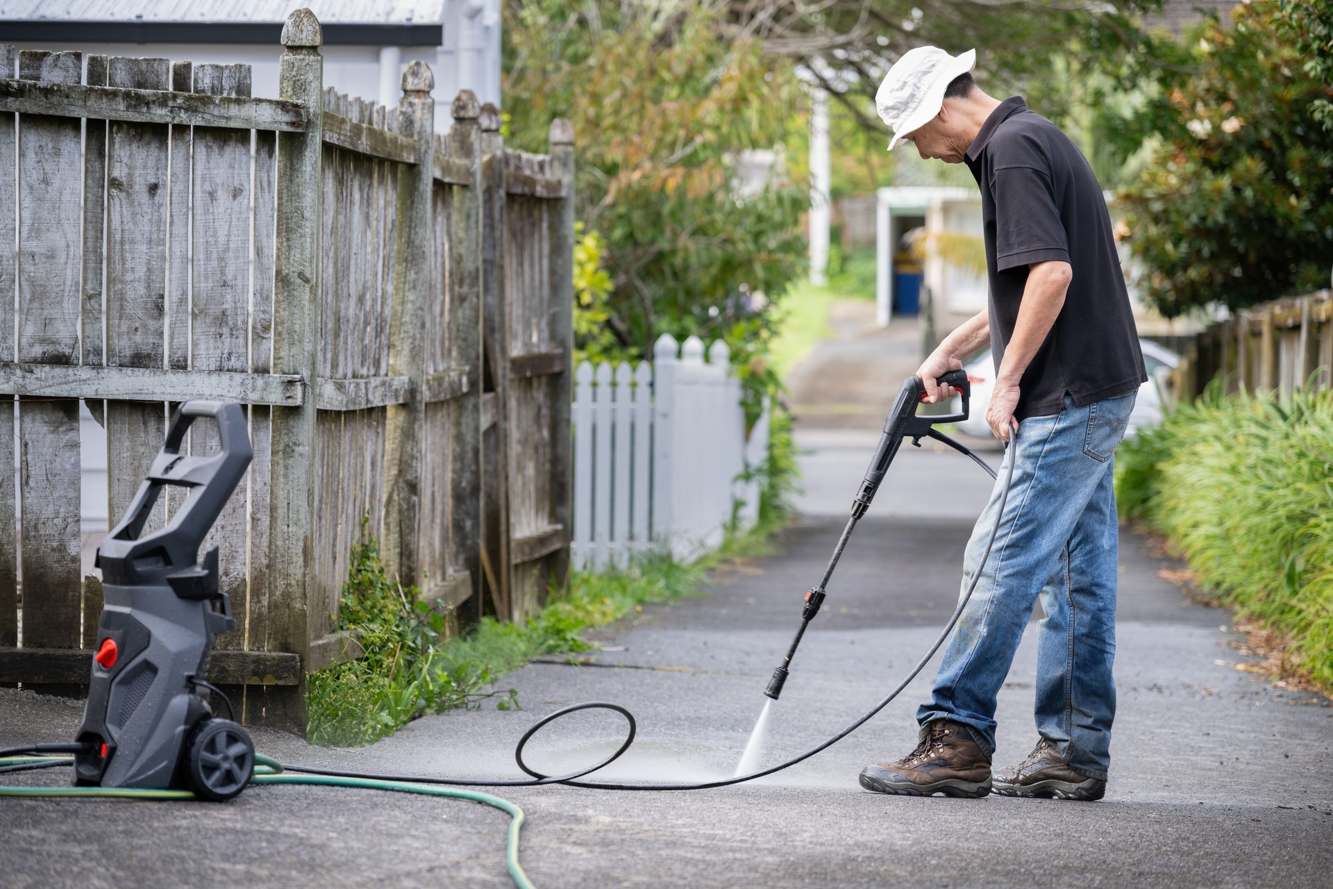 Man cleaning driveway using an electric water blaster.